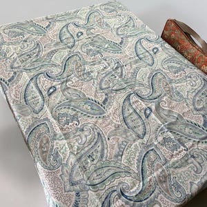 Peut inclure: Une pièce de tissu rectangulaire arborant un motif cachemire dense dans des tons de bleu, vert sauge et beige doux sur un fond blanc. À côté se trouve un petit objet rectangulaire séparé avec un imprimé floral orange et vert vif.