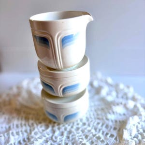 Peut inclure: Trois bols en céramique blanche empilés avec un motif bleu et bleu clair. Le bol supérieur a un bec verseur. Les bols sont empilés les uns sur les autres. Les bols sont sur une surface en dentelle blanche.