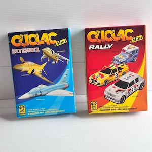 Peut inclure: Deux boîtes de maquettes Cliclac Mini. La boîte bleue Defender présente un Harrier, un Phantom II et un Mirage 2000. La boîte rouge Rally affiche un Super 4x4, une Audi Quattro et une 205 Turbo 16. Les boîtes portent l'indication d'âge 6/9.