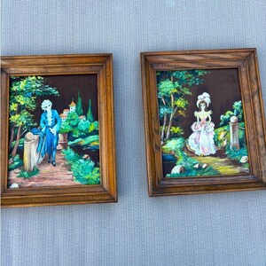 Peut inclure: Deux peintures encadrées dans des cadres en bois. La peinture de gauche montre un personnage en manteau bleu sur un chemin près d'arbres et de bâtiments. La peinture de droite montre un personnage en robe blanche et rose près d'arbres et d'une colonne.