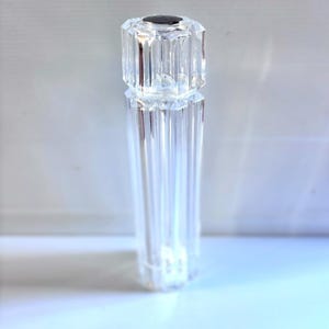 Peut inclure: Un moulin à sel ou à poivre en cristal clair et facetté. Le dessus est de couleur gris foncé. Le corps est de forme cylindrique et long avec des arêtes verticales. Le moulin est en cristal clair et reflète la lumière.
