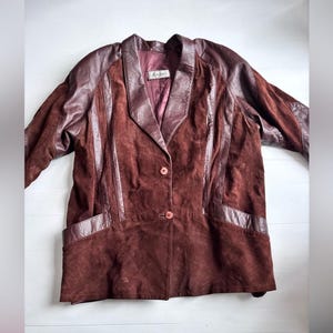 Peut inclure: Un blazer vintage en daim marron avec des empiècements en cuir sur les épaules, le col et les poches. Le blazer a une fermeture à deux boutons et un revers cranté. La doublure est de couleur bordeaux foncé. L'étiquette indique "Kenyon".