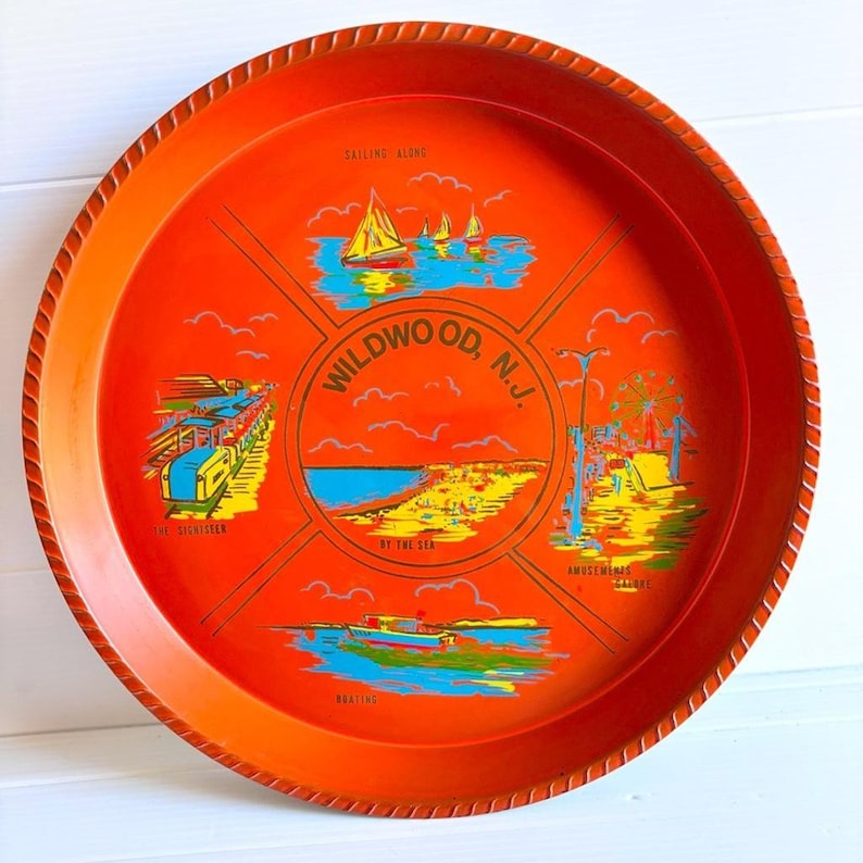 May include: Round orange serving tray with a rope-like edge. The tray features colorful illustrations of Wildwood, N.J., including sailboats, a beach scene, a train, and an amusement park. Text includes "Wildwood, N.J."