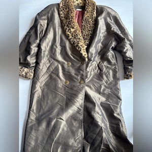 Op de afbeelding: Lange, metallic bronzen jas met een luipaardprint kraag en manchetten. De jas heeft een dubbelborstig ontwerp met twee rijen gouden knopen en twee voorzakken. Vintage stijl.