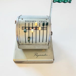 May include: Vintage Paymaster cash register in a light green and silver color scheme. The register features a green handle, dollar and cent indicators, and a "Locked Protection" label. The word "Paymaster" is printed on the base.