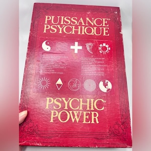 Peut inclure: Boîte de jeu de société vintage rouge avec le titre "PUISSANCE PSYCHIQUE" en lettres dorées. La boîte présente divers symboles et du texte en anglais et en français, dont "PSYCHIC POWER".