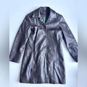 Peut inclure: Un manteau en cuir marron foncé doté d'un col classique, de manches longues et d'une fermeture boutonnée sur le devant avec quatre boutons visibles. Le vêtement présente une finition lisse et une silhouette structurée avec des coutures verticales.