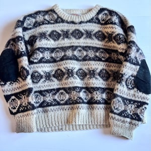 Peut inclure: Un pull vintage en laine crème, noir et marron avec un motif géométrique. Le pull présente des coudières en daim noir et un ourlet et des poignets côtelés. Le design comprend des bandes horizontales avec des motifs de diamants et floraux.