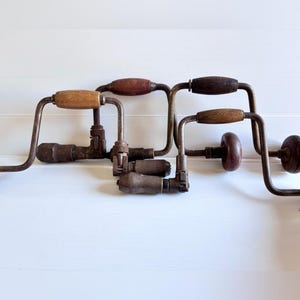 Puede incluir: Un conjunto de taladros manuales antiguos. Están hechos de metal y madera, con mangos de madera en varios tonos de marrón. Las partes metálicas muestran signos de desgaste y óxido, lo que indica su antigüedad. Herramientas vintage.