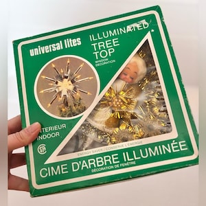 Peut inclure: Un ancien sommet de sapin de Noël dans sa boîte d'origine. La boîte verte porte les mots "universal lites" et "illuminated tree top". Le sommet est un ange avec des accents dorés et une lumière en forme d'étoile. La boîte indique "window decoration".
