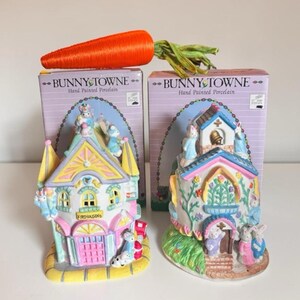 Peut inclure: Deux bâtiments en porcelaine peints à la main Bunny Towne avec leurs boîtes d'origine. L'un est une caserne de pompiers avec des portes roses et des tourelles jaunes, l'autre une église avec un clocher. Ils présentent des figurines de lapins.