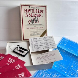 Könnte beinhalten: Eine How to Host a Murder Krimispiel-Box mit dem Titel The Watersdown Affair, die eine Kassette, einen Bogen mit Namensschildern, ein gedrucktes Testament und blaue Grundrisspläne auf einer weißen Oberfläche enthält.