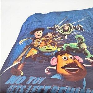 Puede incluir: Una colcha azul con personajes de la pel&iacute;cula de animaci&oacute;n Toy Story. El dise&ntilde;o incluye a Woody, Buzz Lightyear, Rex, los Aliens y el Sr. Potato. El texto "NO TOY GETS LEFT BEHIND" est&aacute; impreso en la parte inferior.