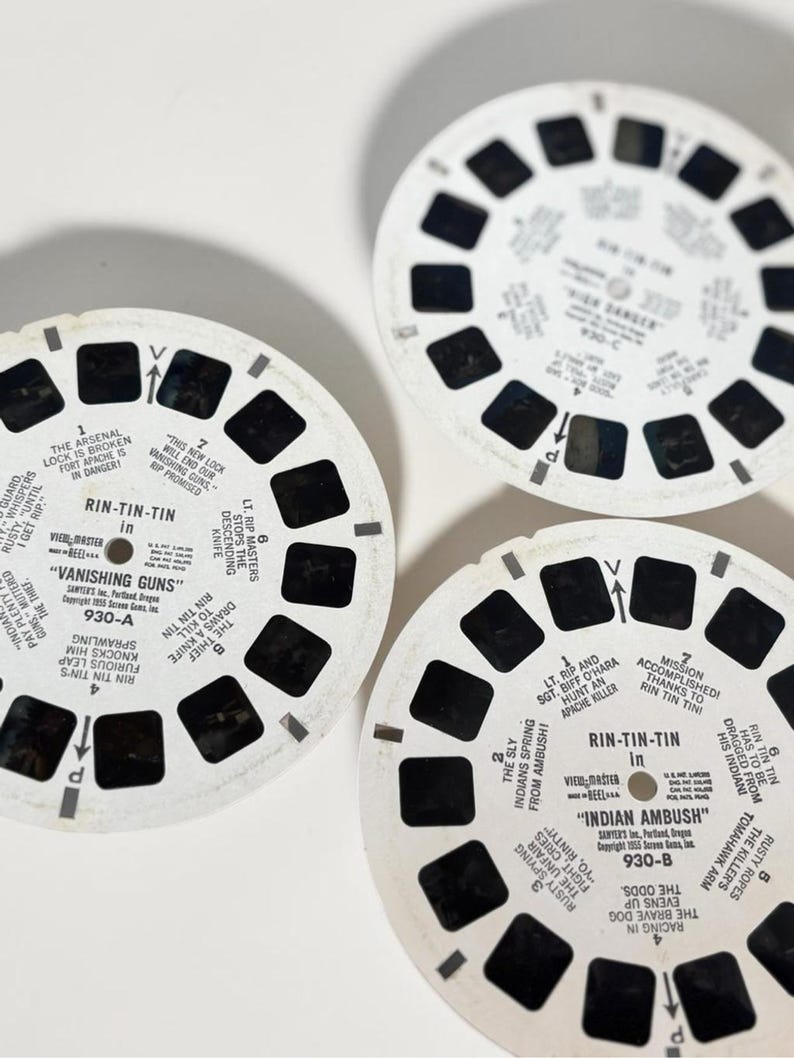 May include: Three vintage View-Master reels with black and white images and text. The reels feature the text "Rin-Tin-Tin" and titles like "Vanishing Guns" and "Indian Ambush". Each reel has a series of small, square viewing windows.