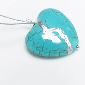 May include: A turquoise heart-shaped pendant with a silver crackle design. The pendant is attached to a silver chain.