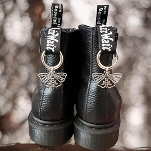 Peut inclure: Bottines noires en cuir à lacets avec des breloques en forme de papillon argentées. Les breloques portent l'inscription "With soles bouncing".