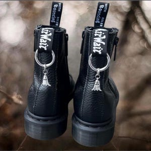 May include: Pair of black leather ankle boots with silver ghost charms hanging from the back loops. The boots have a textured finish and black soles. The back loops feature the words "Air Wair" and "With Bouncing Soles" in white.