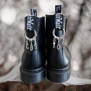 May include: Black leather ankle boots with zipper closures and silver charms that spell "CUSTOM" and "TOM" hanging from the laces.