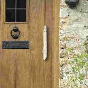 May include: A wooden door with a small window and a black metal knocker. The door is set in a stone wall, with a sign that reads "THE CORNER HOUSE". A black lantern hangs on the wall.