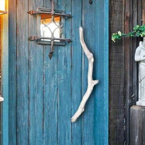 Peut inclure: Une porte en bois bleu sarcelle avec une poignée en métal rustique et une petite fenêtre avec une grille en métal. La porte est entourée de bardage en bois et de verdure.