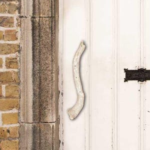 May include: A distressed white wooden door with vertical panels, a curved silver handle, and a black letterbox. The door shows signs of wear with peeling paint. The door is framed by stone columns and set against a brick wall.