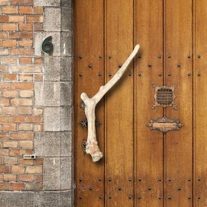 May include: A wooden door with a unique antler door handle. The door is set in a brick wall with a stone frame. The door is brown and has a weathered look.