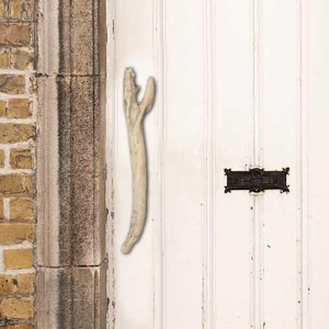 May include: A white wooden door with a weathered finish and a unique bone-shaped door handle. The door has a small black metal letterbox with a rectangular opening.