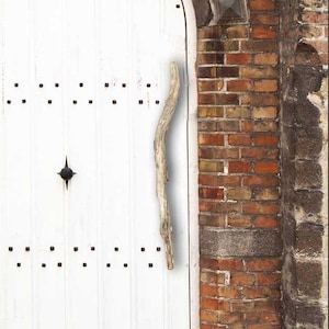 May include: A white wooden door with a rustic wooden handle. The door is set in a brick wall with a stone archway.