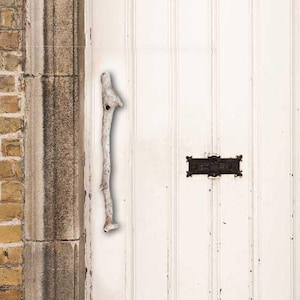 May include: A white wooden door with a weathered finish and a natural wood door handle. The door has a black metal letterbox with a rectangular shape.