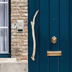 May include: A blue front door with a brass door knocker and a gold letterbox. The door is surrounded by brick and has a small, decorative, wooden branch on the left side.