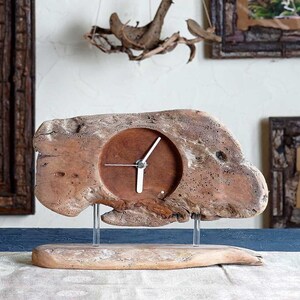 May include: A wooden clock with a round face and white hands. The clock is mounted on a piece of driftwood with a natural, rustic finish. The clock is sitting on a wooden base.