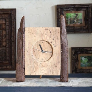 May include: A wooden clock with a rustic design. The clock face is surrounded by a circular frame and has black hands. The clock is standing on a wooden base with two wooden pillars on either side.