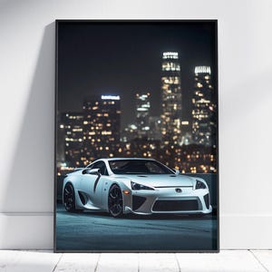 May include: A white Lexus LFA supercar parked in front of a city skyline at night. The car is facing the camera and the city lights are blurred in the background.