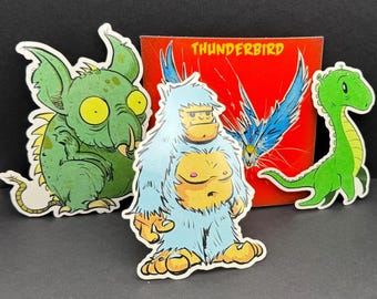 May include: Three colorful stickers featuring cartoon illustrations of a green monster, a blue yeti, and a green dinosaur. The stickers are on a red background with the word "THUNDERBIRD" printed in white.