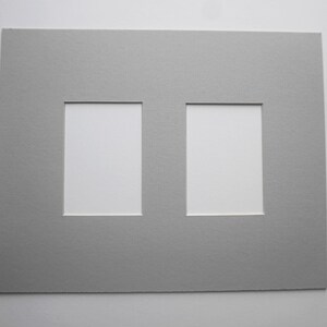 May include: A gray picture mat with two rectangular openings. The mat is made of textured paper and is designed to hold two photos or artworks. The openings are white.