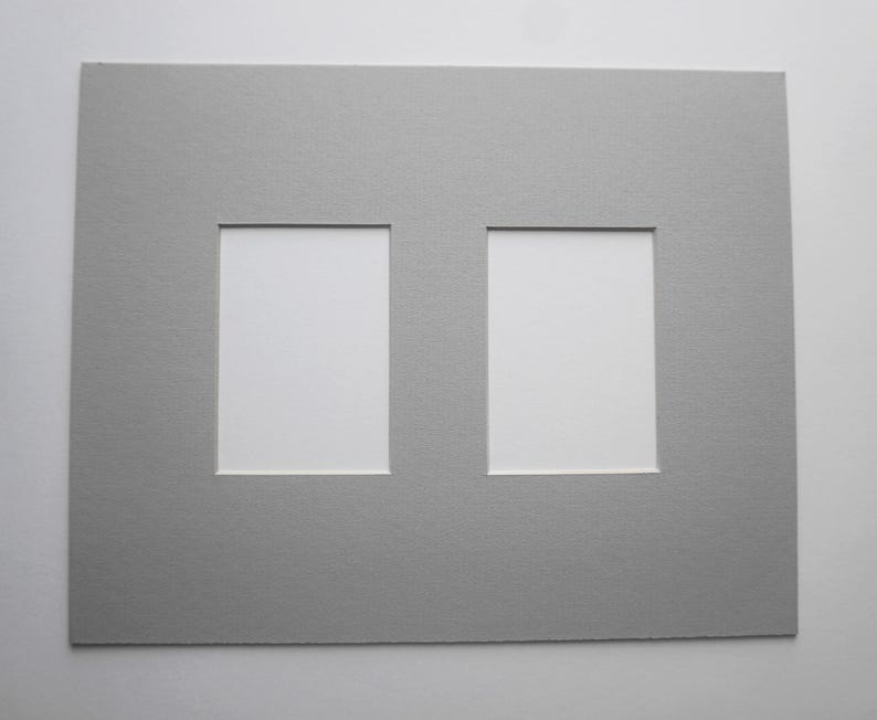 May include: A gray picture mat with two rectangular openings. The mat is made of textured paper and is designed to hold two photos or artworks. The openings are white.