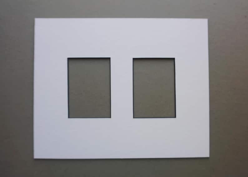 May include: A white picture mat with two rectangular openings. The mat is made of thick, bright white paper and is set against a neutral gray background. The openings are evenly spaced and have a black border.