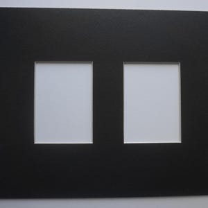 May include: A black picture mat with two rectangular openings. The mat has a textured surface and white backing visible through the openings. Ideal for displaying two photos or artwork.