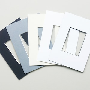 May include: Five different colored mat boards with a rectangular opening in the center. The mat boards are arranged in a fan shape, with the darkest color at the bottom and the lightest color at the top. The colors are navy blue, light blue, cream, white, and off-white.