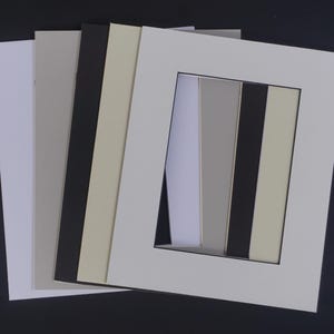 May include: A set of eight mat boards in various colors, including white, cream, gray, and black. The mat boards are arranged in a stack, with the largest mat board on the bottom and the smallest mat board on top. The mat boards have a rectangular opening in the center.