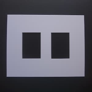 May include: A white picture mat with two rectangular openings. The mat is square and has a clean, minimalist design. The background is a dark gray color, providing contrast to the white mat.