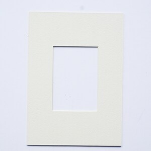 May include: A white mat with a rectangular opening in the center. The mat is designed to be used for framing photographs or artwork.