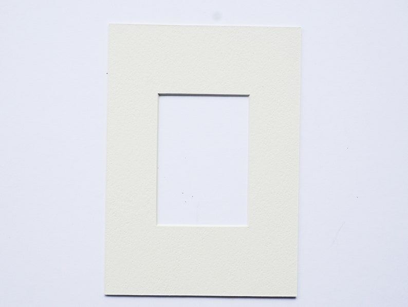 May include: A white mat with a rectangular opening in the center. The mat is designed to be used for framing photographs or artwork.