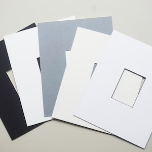 May include: Five different colored mat boards with a rectangular opening in the center. The mat boards are black, white, gray, light gray, and cream.
