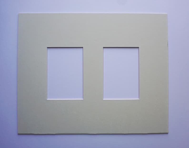 May include: A light green double picture mat with two rectangular openings. The mat is made of thick paper and has a clean, simple design. The openings are white, ready for photos or artwork.