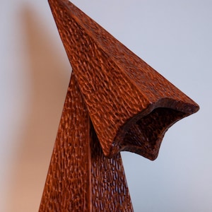 May include: A unique, handcrafted wooden lamp with a textured surface. The lamp features a geometric design with a star-shaped shade and a triangular base. The warm brown color and intricate carving create a striking visual effect. The lamp is a decorative lighting fixture.