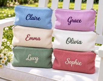 Puede incluir: Seis estuches rectangulares acanalados con cremallera en azul claro, lavanda, crema, blanco, verde salvia y rosa. Cada estuche tiene un nombre bordado en letra cursiva: Claire, Grace, Emma, Olivia, Lucy y Sophie, con cremalleras plateadas.