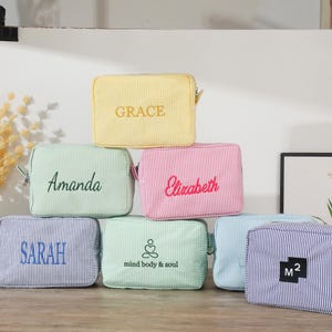 May include: Six different patterned zippered pouches with various embroidered names and phrases. The pouches are yellow, green, pink, blue, and white.