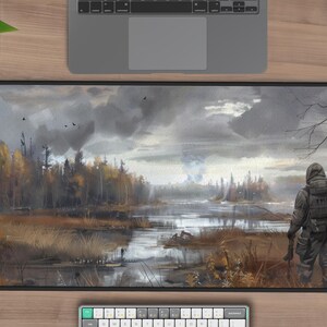 May include: A gray and brown landscape painting with a figure in a black jacket and a backpack standing in the foreground. The figure is looking out at a lake in the distance. The sky is cloudy and gray.