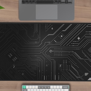 May include: A black mouse pad with a white circuit board design. The mouse pad is on a wooden desk with a laptop, a cup of coffee, and a white wireless mouse.